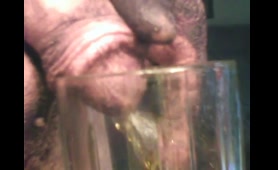 Old dude pours a long piss stream into a glass on the couch